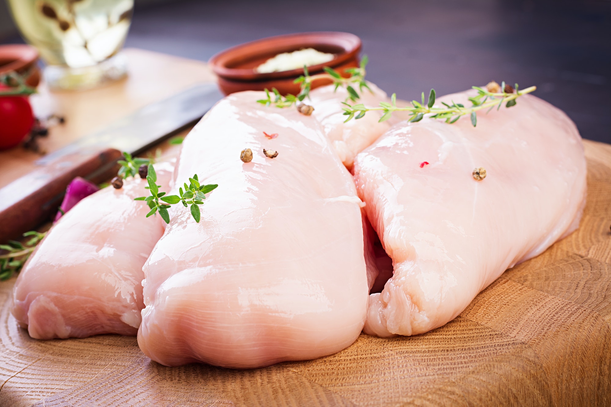 Raw chicken breast fillets on wooden cutting board with herbs and spices.